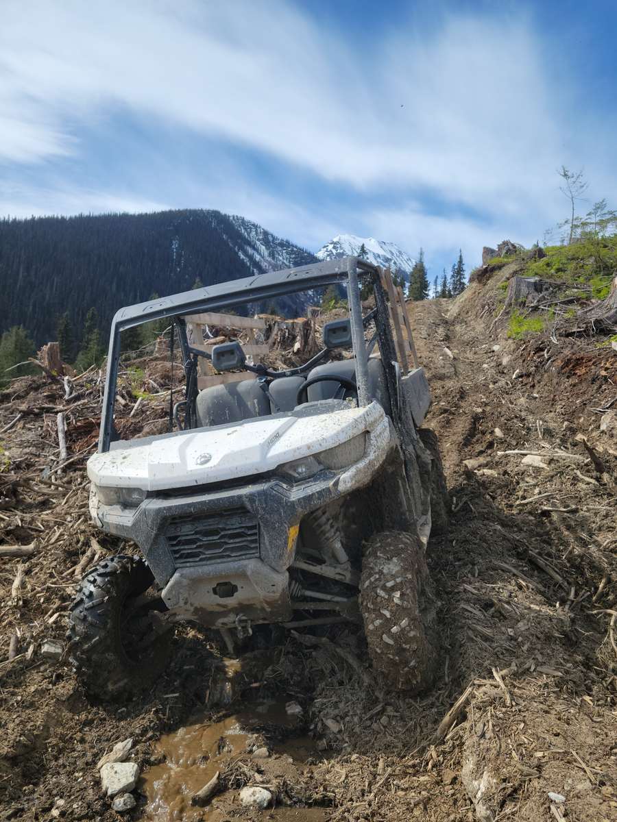 Side-by-side utility vehicle on a muddy skid road below a snow-capped peak